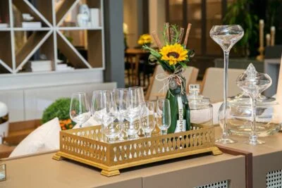 Espumante Chandon com Girassol dentro da garrafa que está dentro de cercado de madeira com taças transparentes.